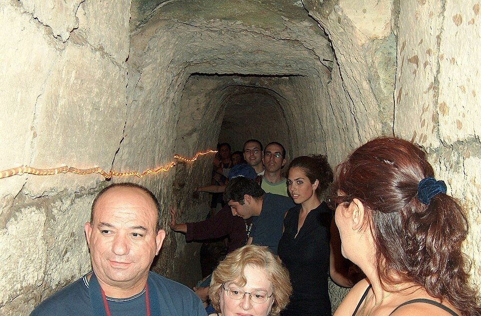 מטיילים צועדים במים בתוך מנהרת אמת המים העתיקה במי קדם, פארק אלונה